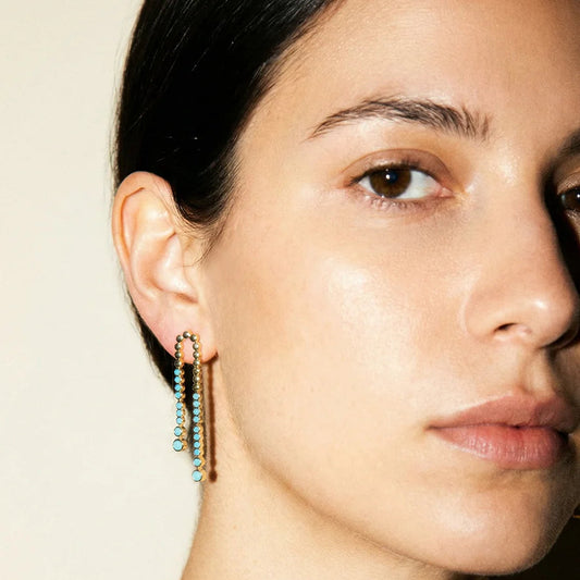 Close-up of a woman wearing gold earrings with green beads on a neutral background