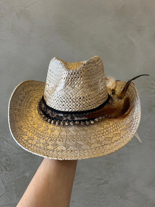 Straw cowboy hat with decorative band and feather held against a gray background
