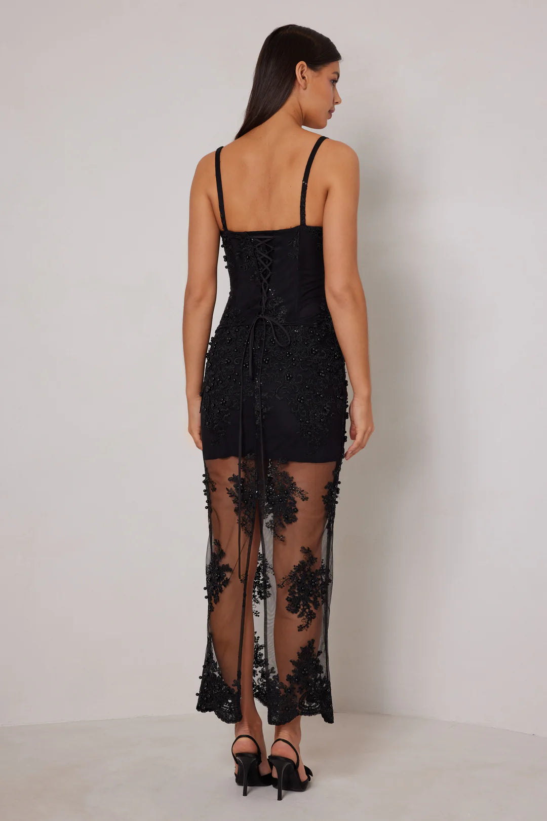 Woman wearing a black lace dress with sheer panels on a white background