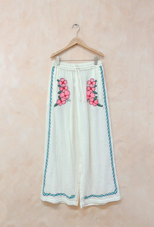White pants with pink floral embroidery on a beige background
