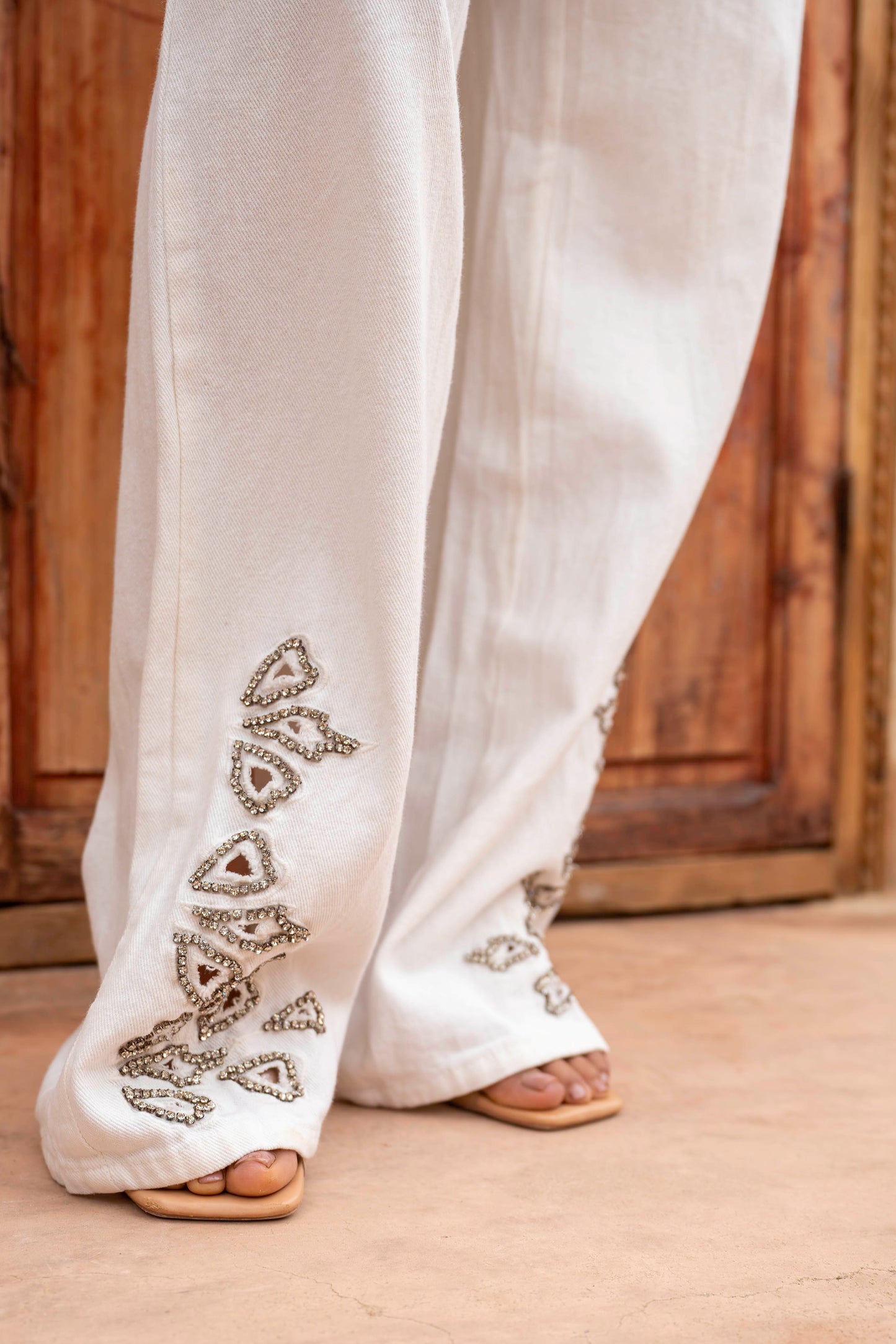 White pants with intricate black embroidery on a wooden floor.