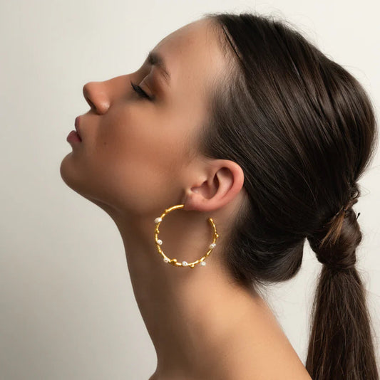 Woman wearing a gold hoop earring against a neutral background
