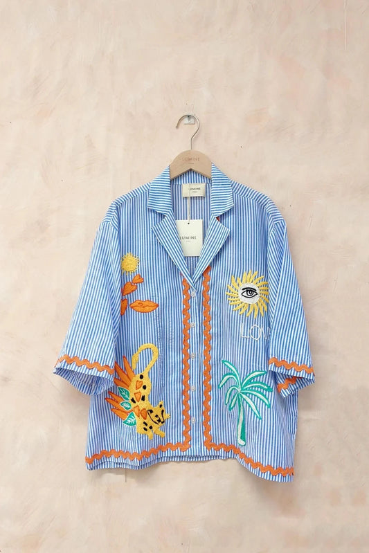 Blue striped shirt with colorful embroidery on a beige background