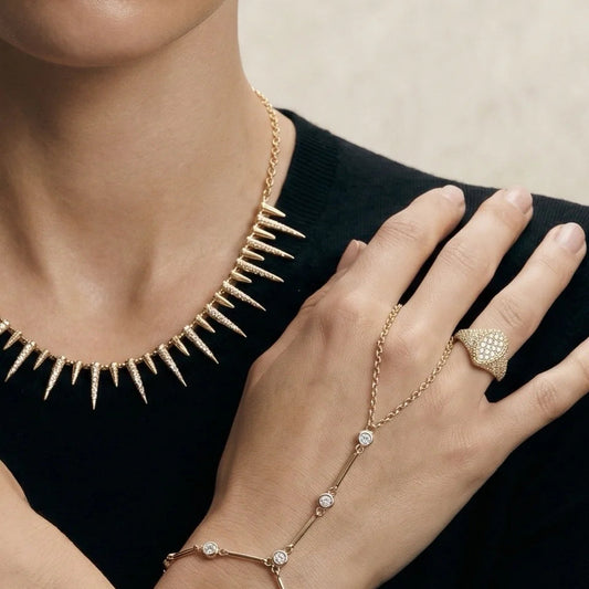 Gold spiked necklace, bracelet, and ring on a person against a neutral background