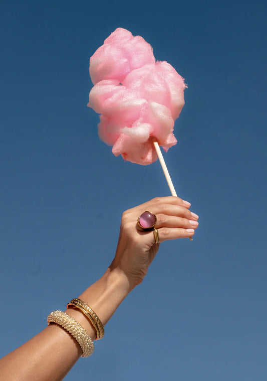 Hand holding pink cotton candy against a clear blue sky