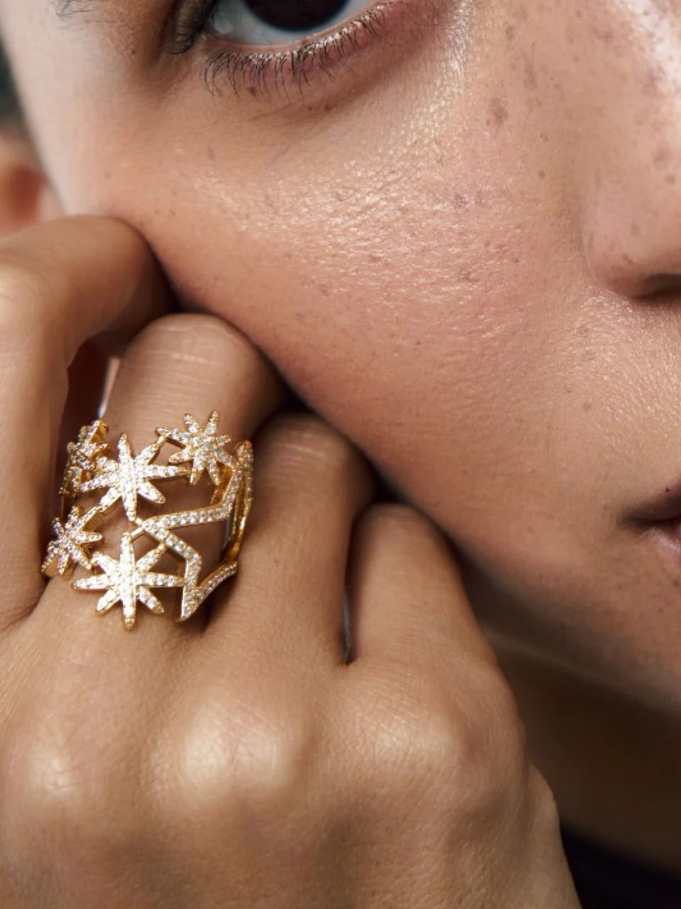 Close-up of a person wearing a gold ring with star designs on their finger.
