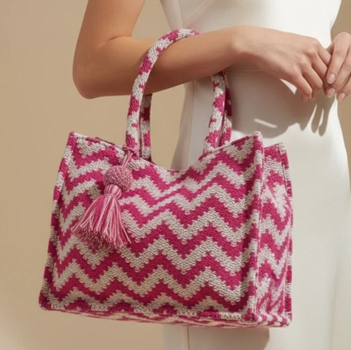 Pink and white zigzag patterned bag with a tassel held by a person against a beige background