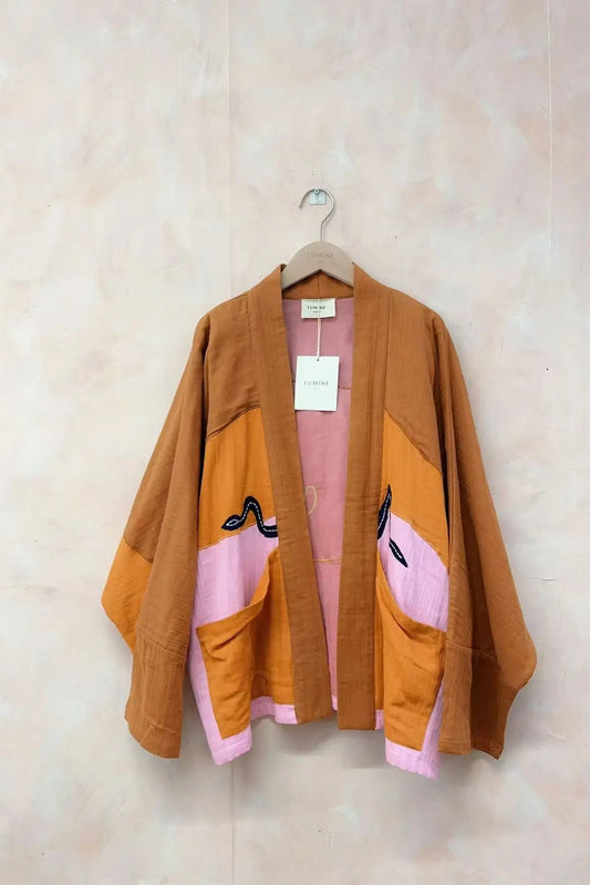 Brown jacket with pink accents on a hanger against a beige wall