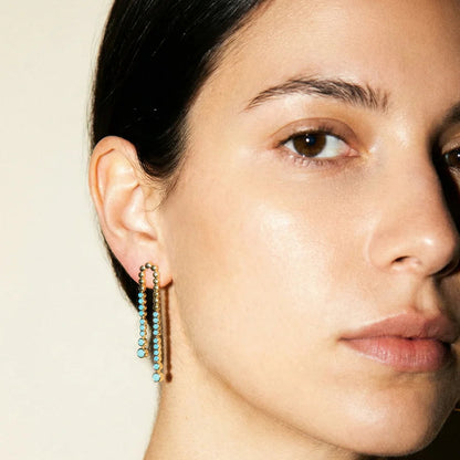 Close-up of a woman wearing gold earrings with green beads on a neutral background