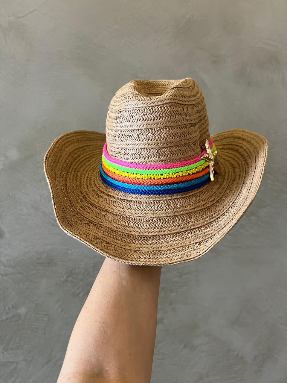 Brown straw hat with colorful band held against a gray background