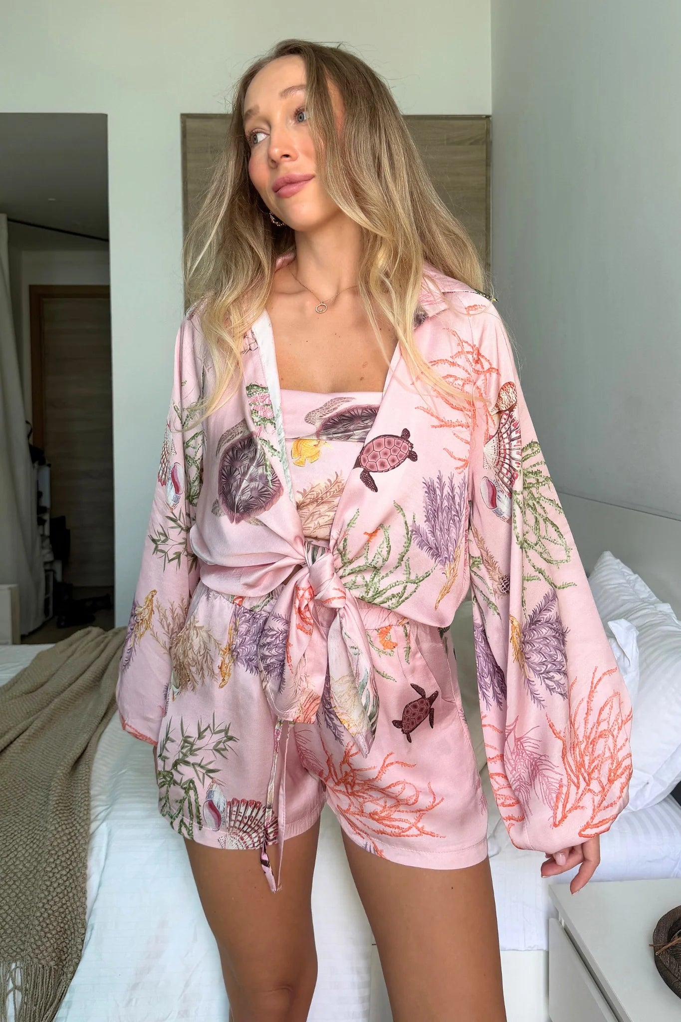 Woman wearing a floral pink robe standing in a bedroom.