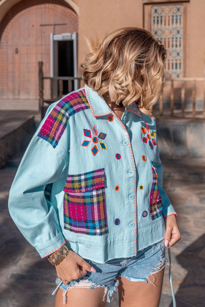 Person wearing a colorful embroidered denim jacket in an outdoor setting.