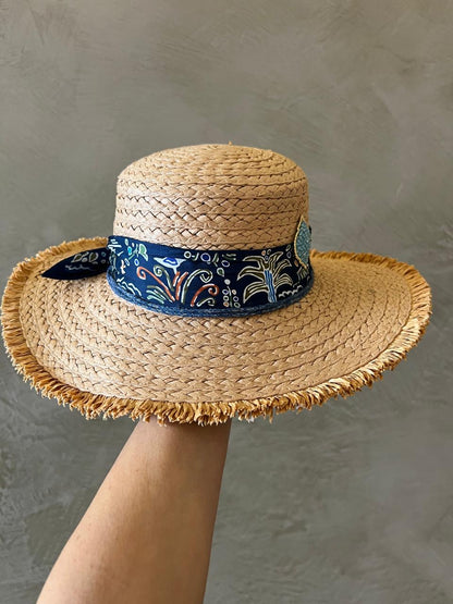 Straw hat with a decorative blue band held against a neutral background