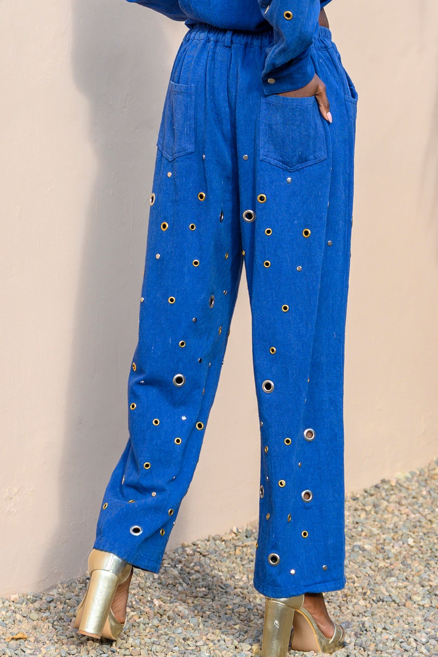 Blue pants with gold embellishments worn by a person against a beige background