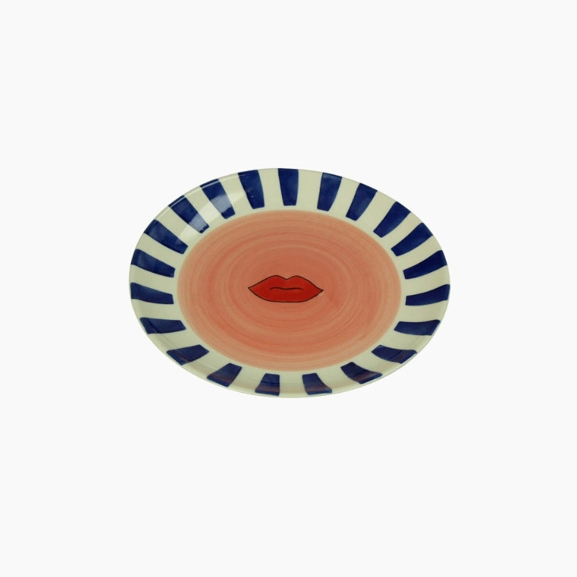 Decorative plate with blue and white stripes and a red lip design on a peach background
