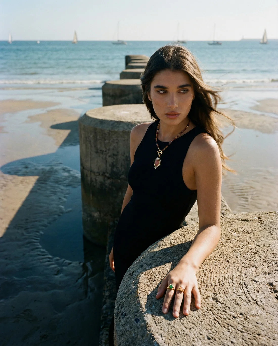 Woman in a black sleeveless top standing on a beach with ocean and sky in the background