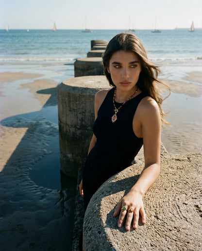 Woman in a black sleeveless top standing on a beach with ocean and sky in the background