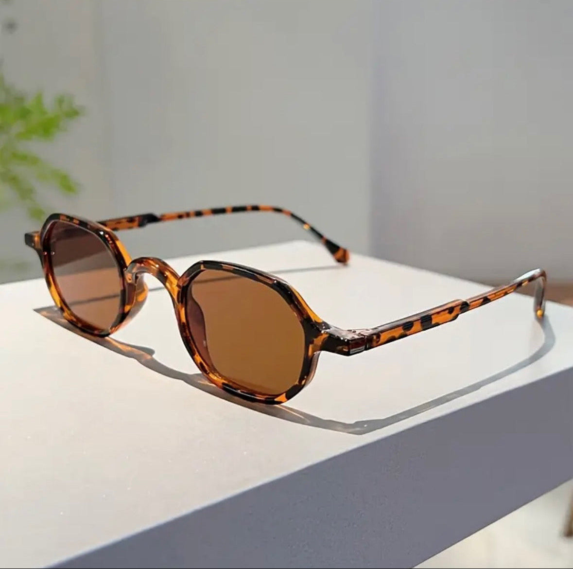 Sunglasses with tortoiseshell frame and brown lenses on a light surface.