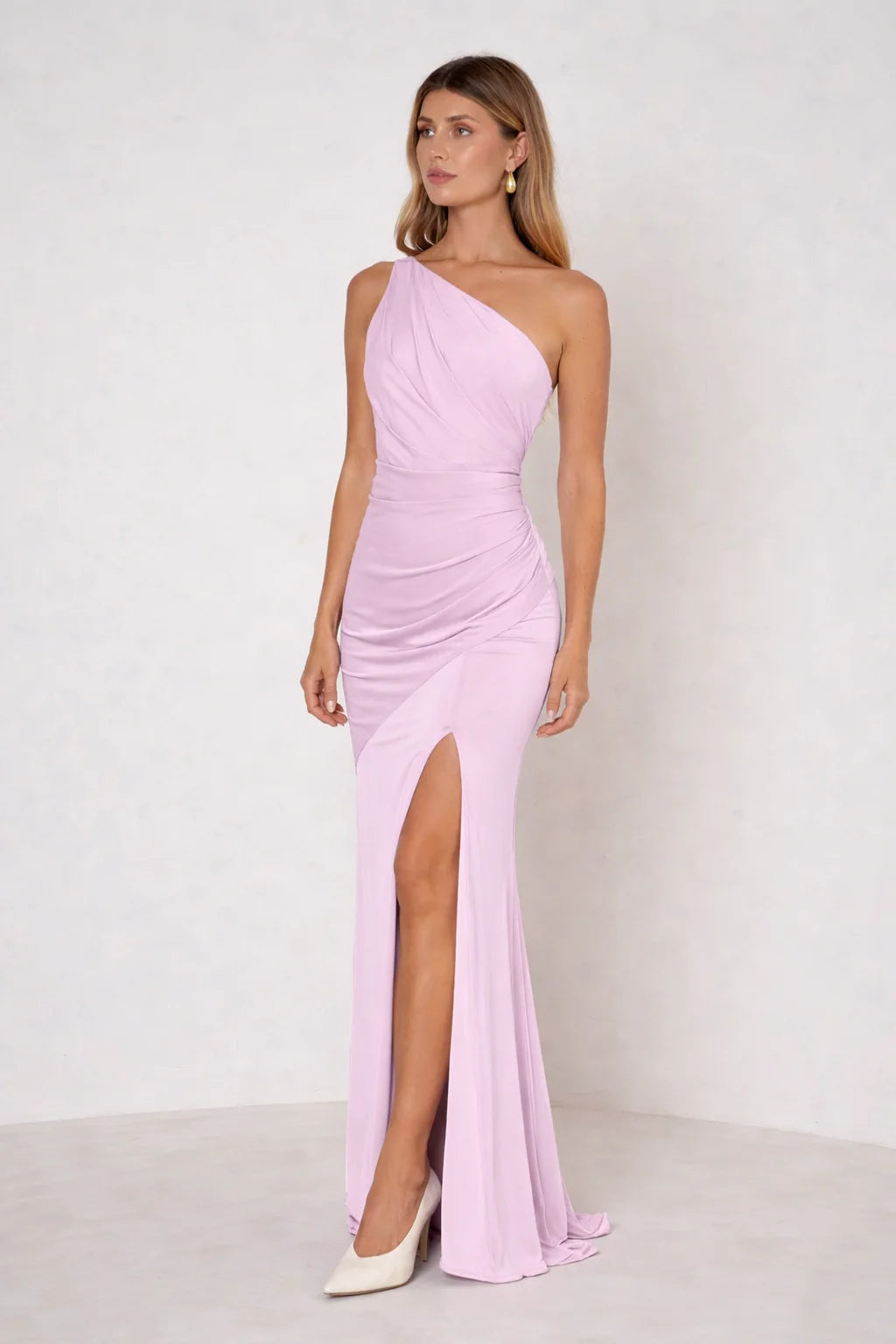 Woman wearing a pink one-shoulder dress with a slit on a white background