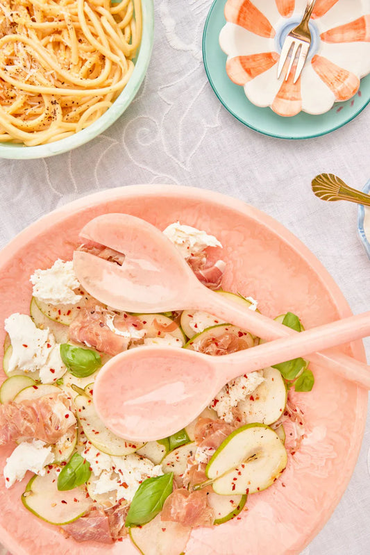 Salad with figs, goat cheese, and basil on a pink plate with wooden spoons.