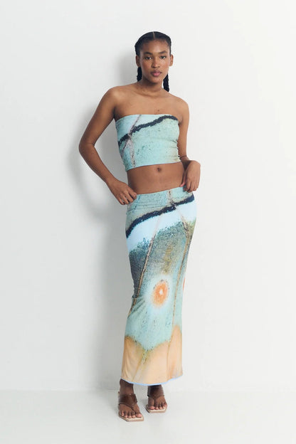 Woman wearing a strapless top and long skirt with abstract design on a white background