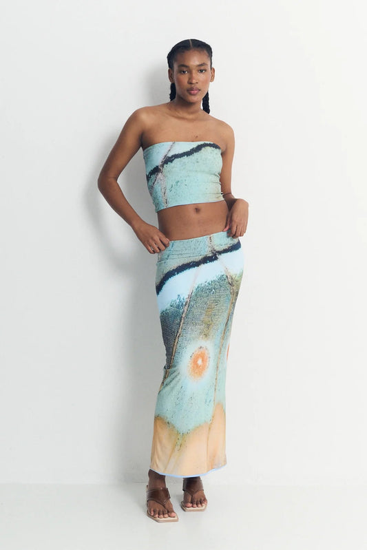 Woman wearing a strapless top and long skirt with abstract design on a white background