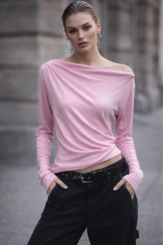 Woman wearing a pink off-shoulder top and black pants against a blurred urban background