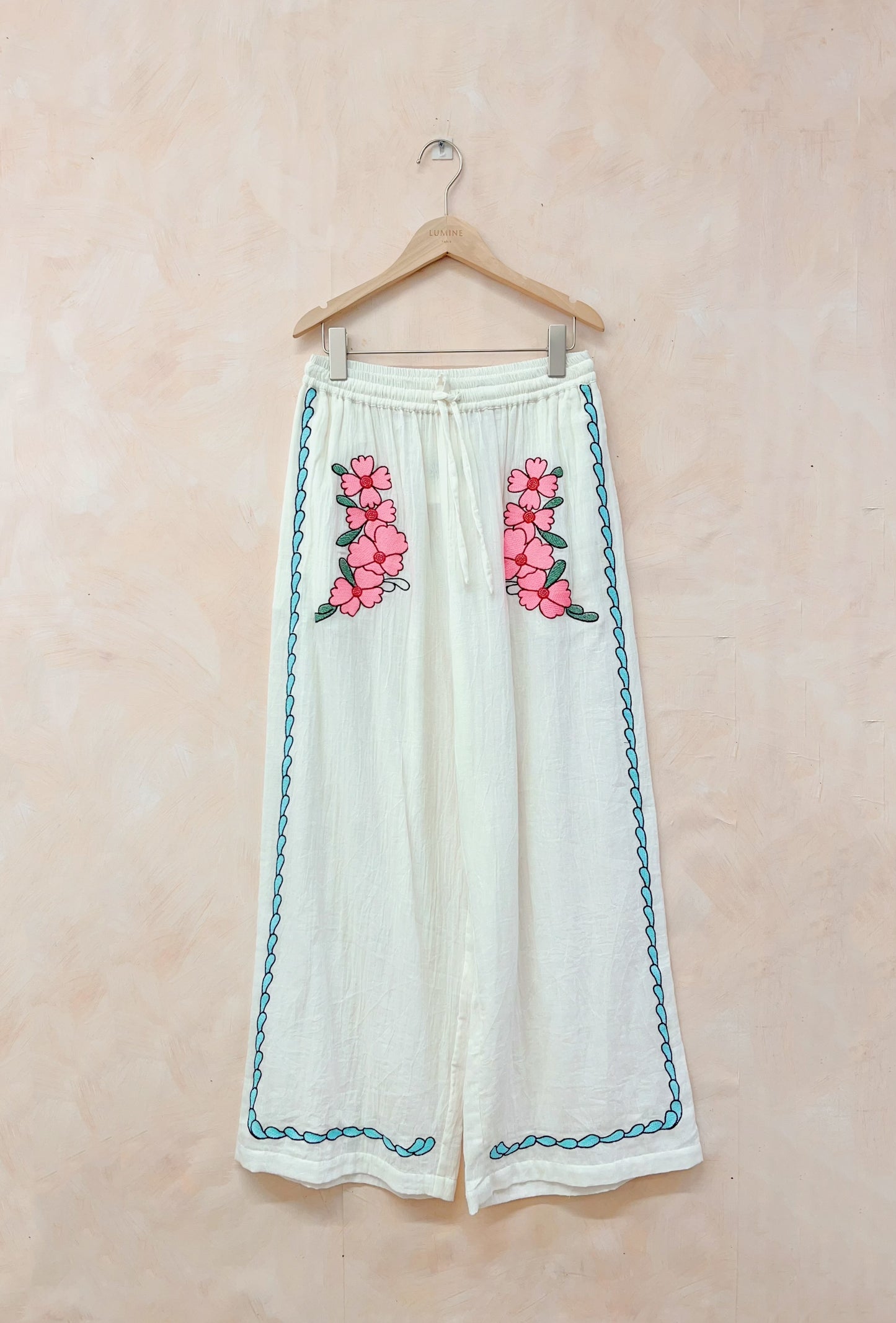 White pants with pink floral embroidery on a beige background