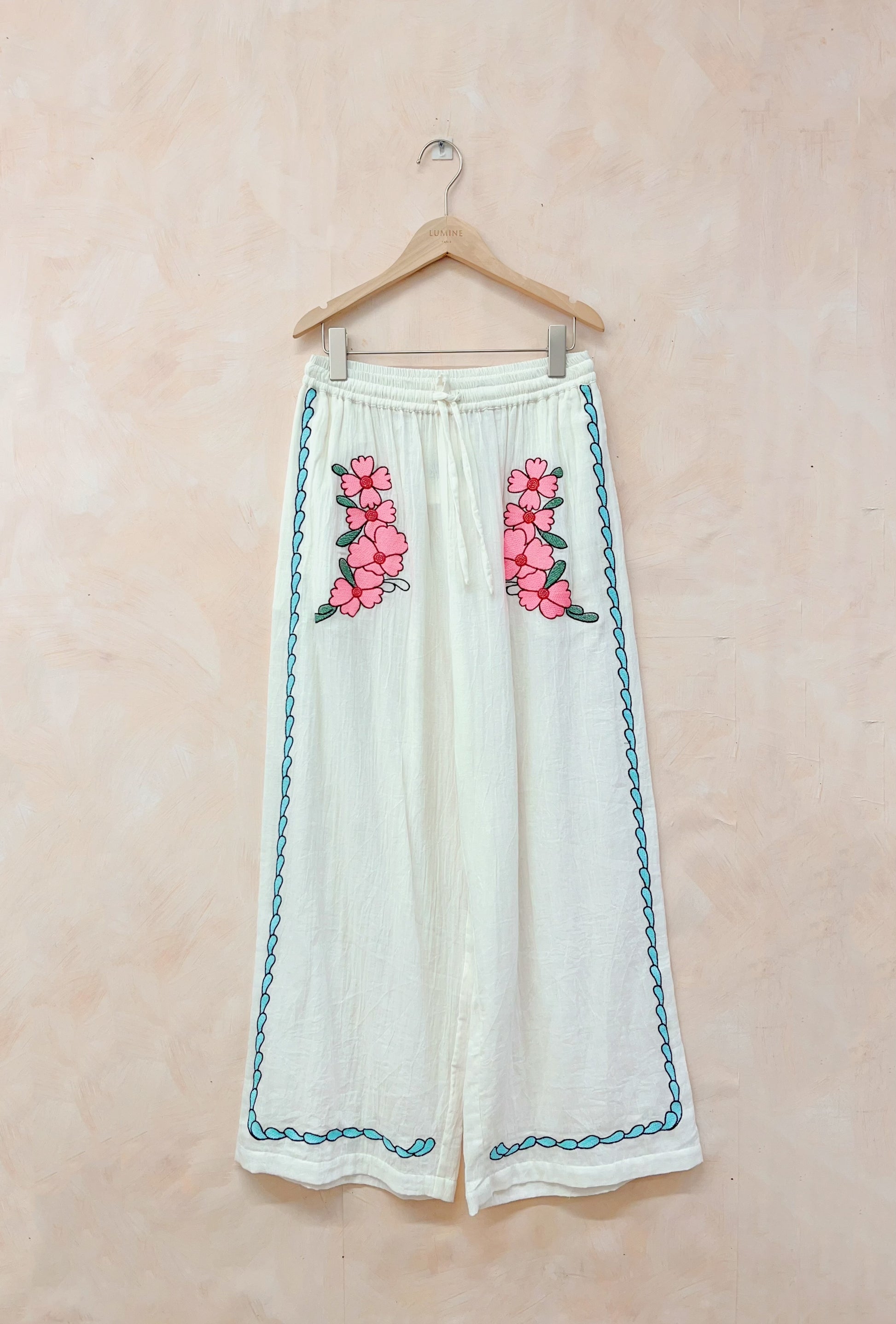 White pants with pink floral embroidery on a beige background