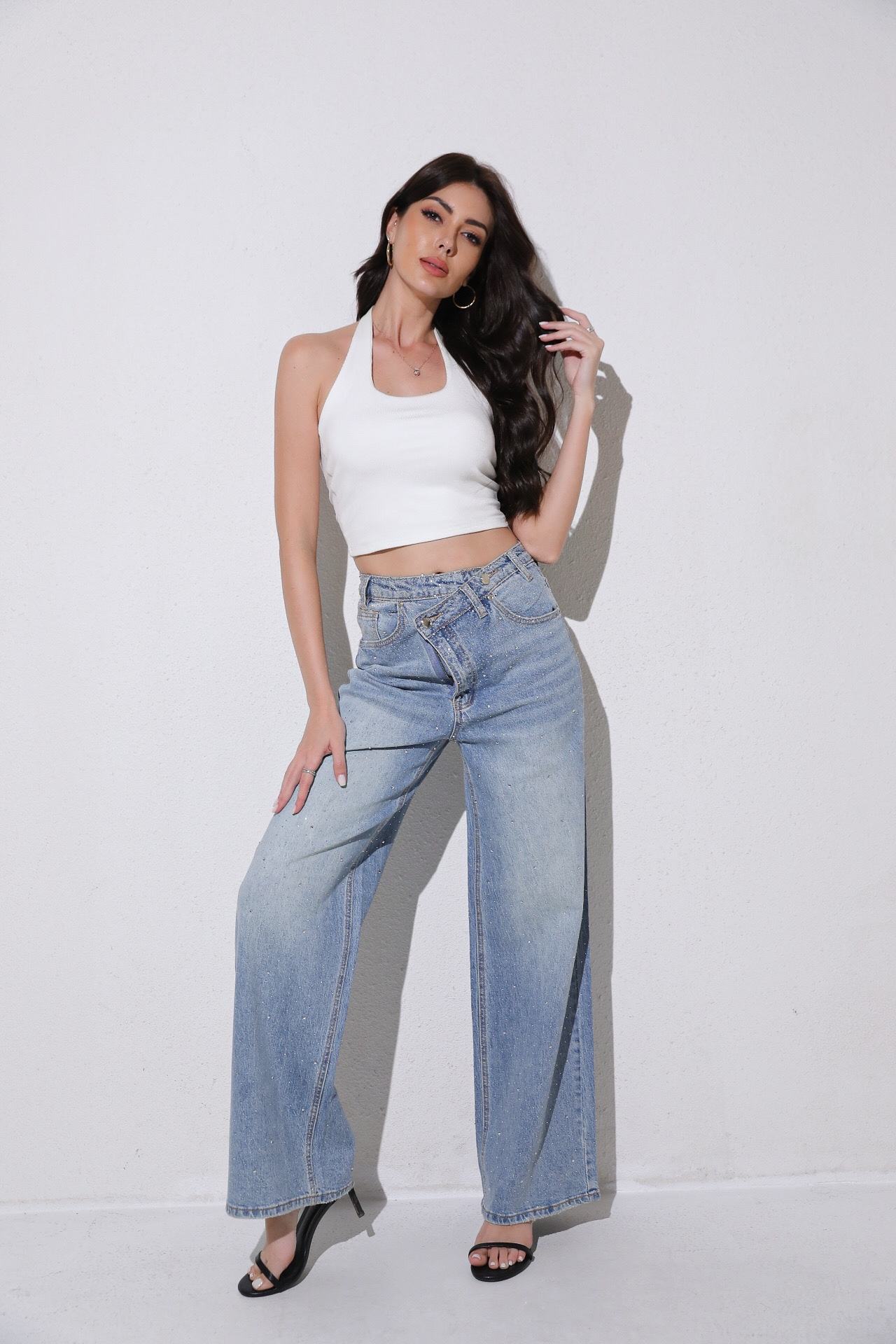 Woman wearing a white crop top and blue jeans against a plain background