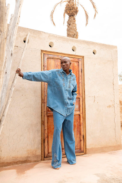 Man in a blue outfit standing in front of a traditional building with a wooden door.