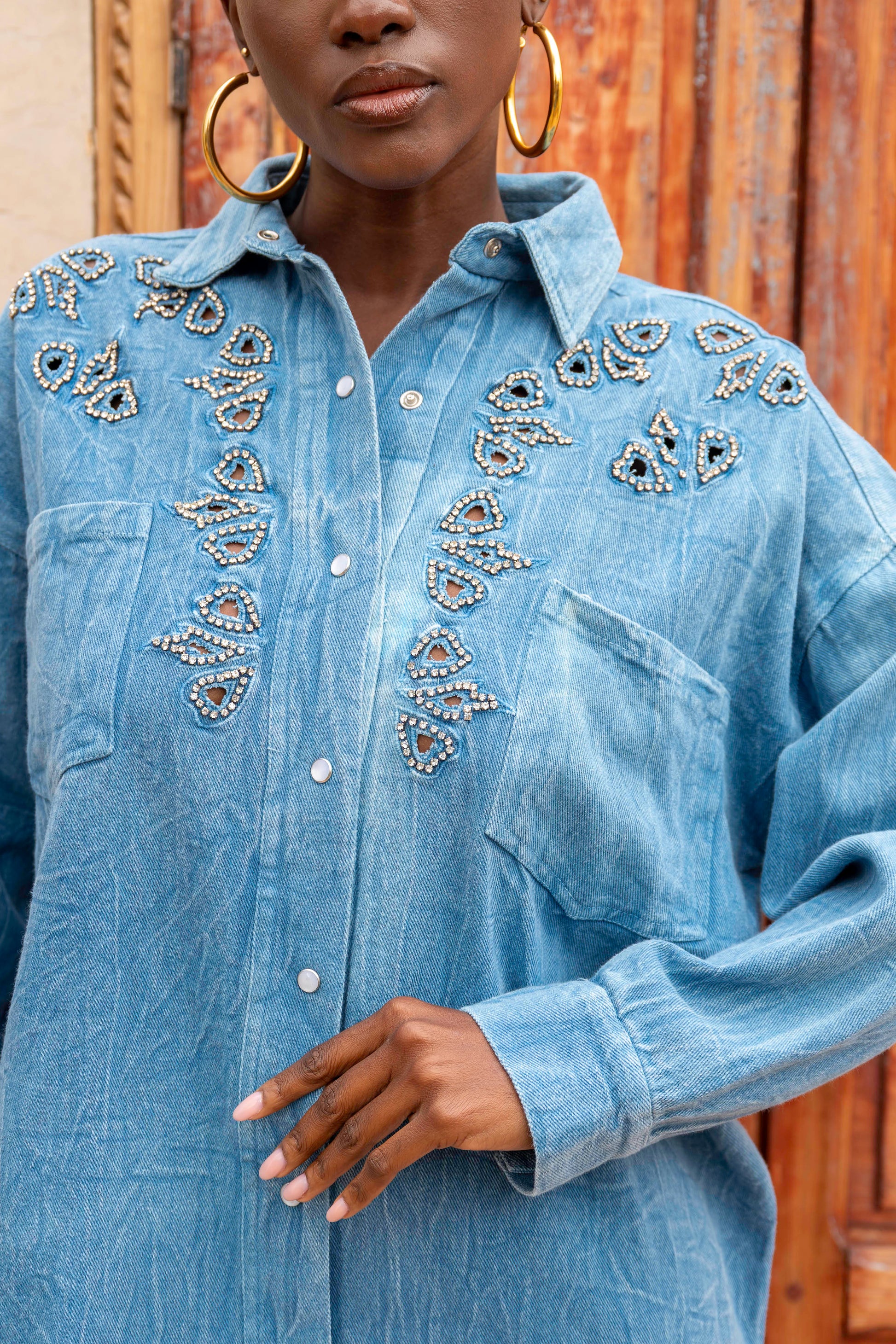 Blue denim shirt with decorative embellishments worn by a person against a wooden background