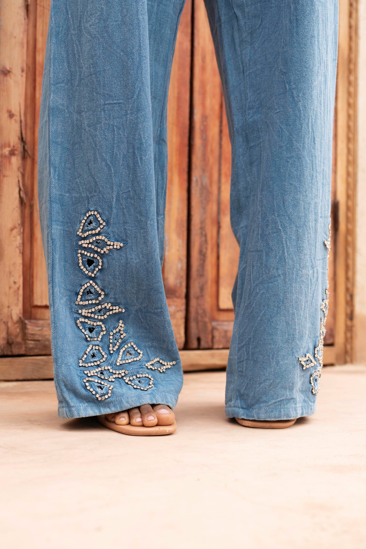 Blue jeans with decorative beadwork on a wooden floor.