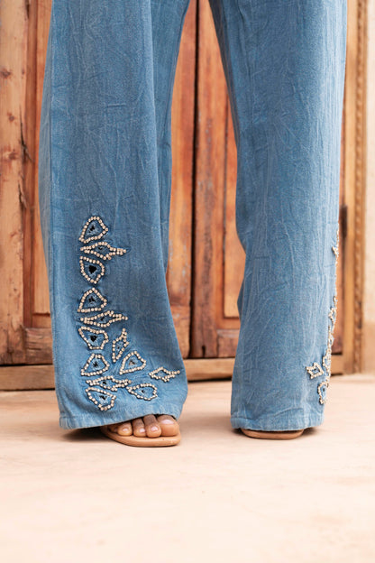 Blue jeans with decorative beadwork on a wooden floor.