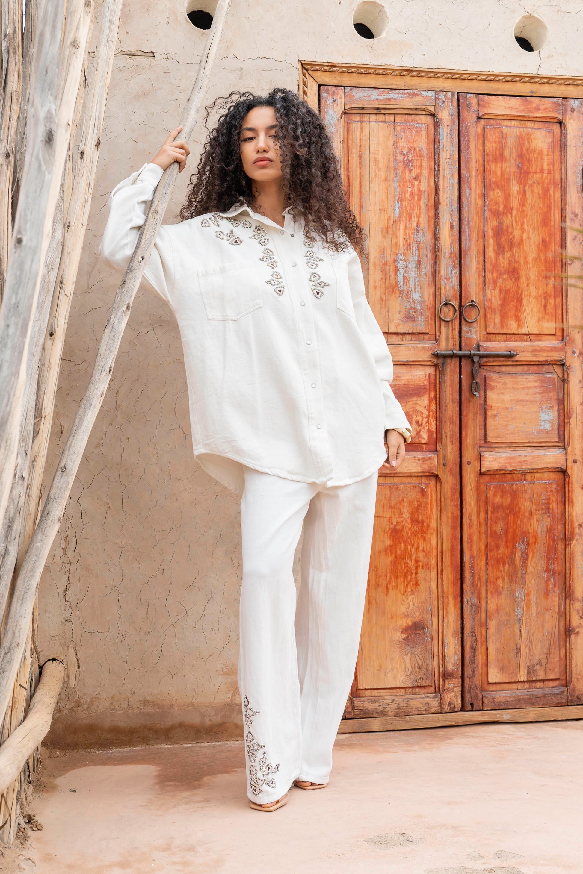 Woman in a white embroidered outfit standing in front of a wooden door.