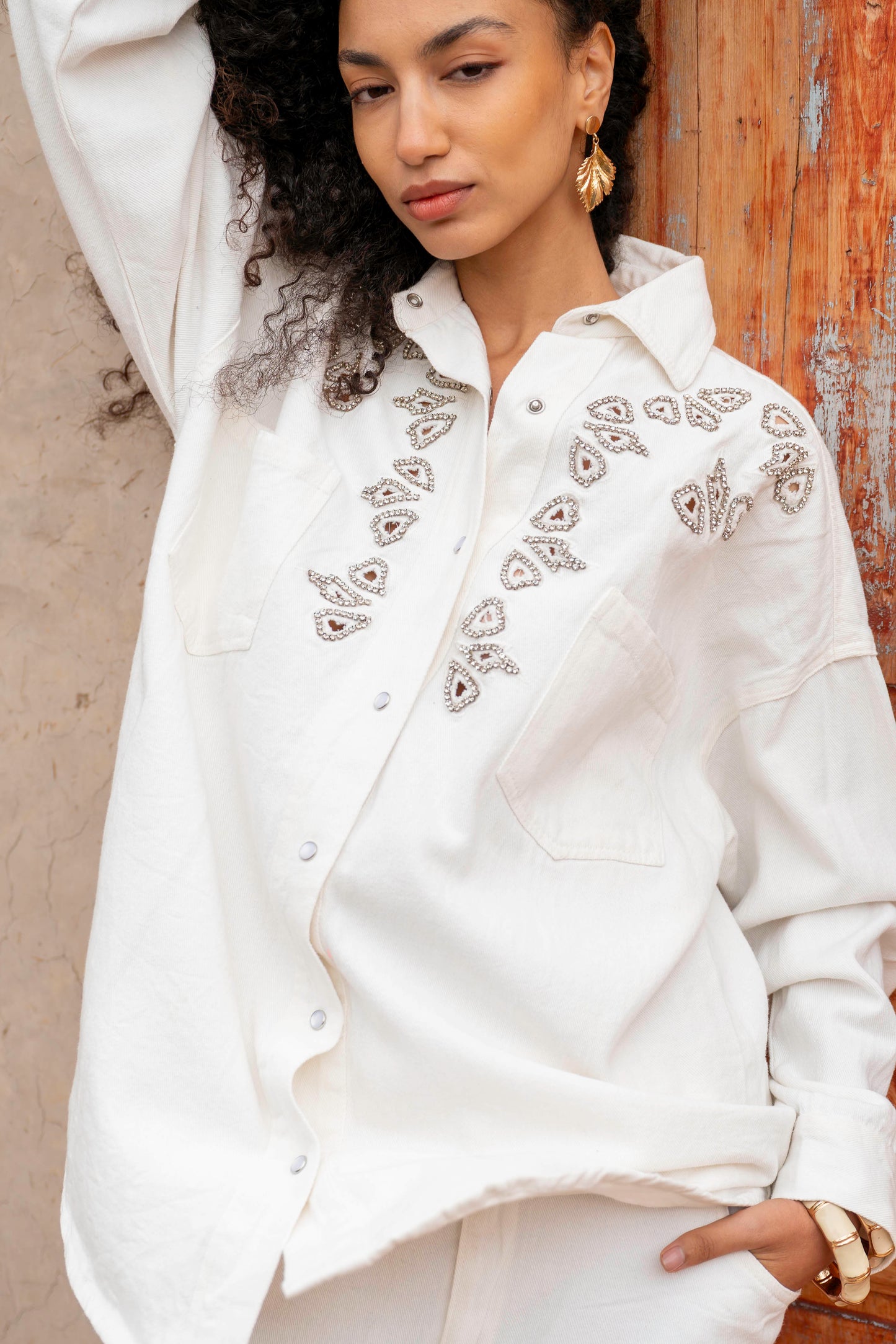 Woman wearing a white embroidered shirt against a textured wall.