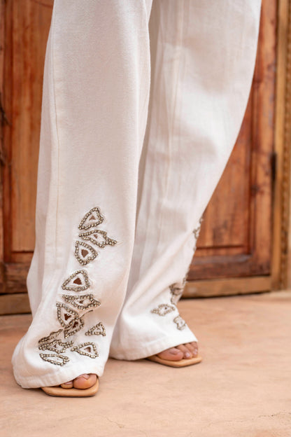 White pants with intricate black embroidery on a wooden floor.