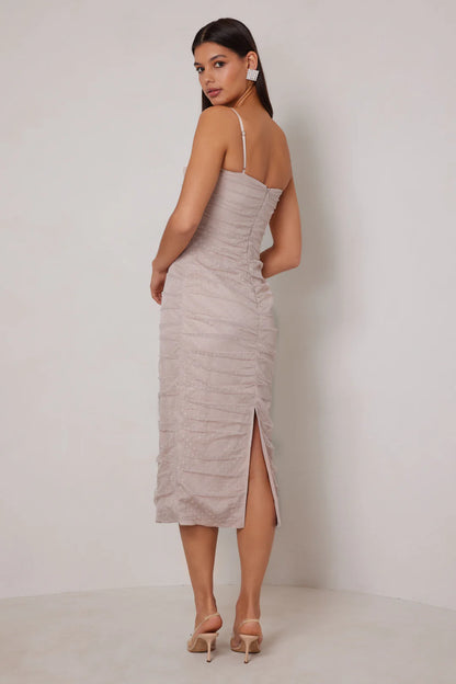 Woman wearing a beige dress with a slit on a plain background