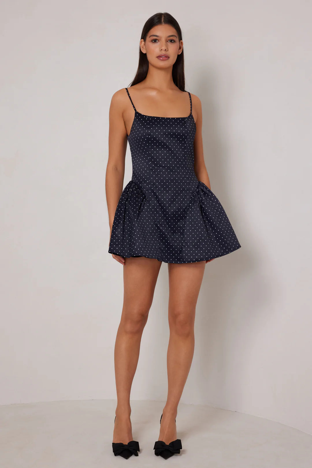 Woman wearing a navy polka dot dress against a white background