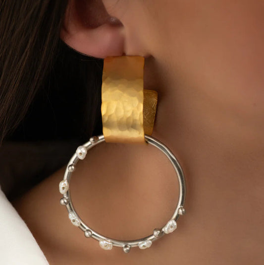 Close-up of a person wearing gold hoop earrings with a blurred background
