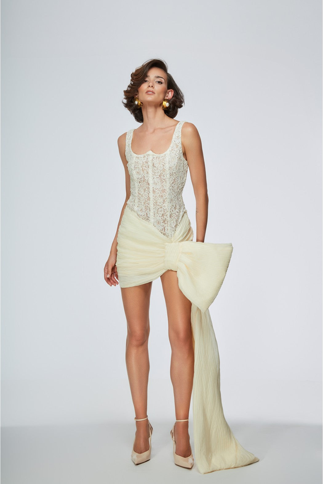 Woman wearing a light green lace dress with a large bow on a white background