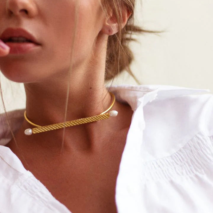 Woman wearing a gold choker necklace with pearls against a neutral background