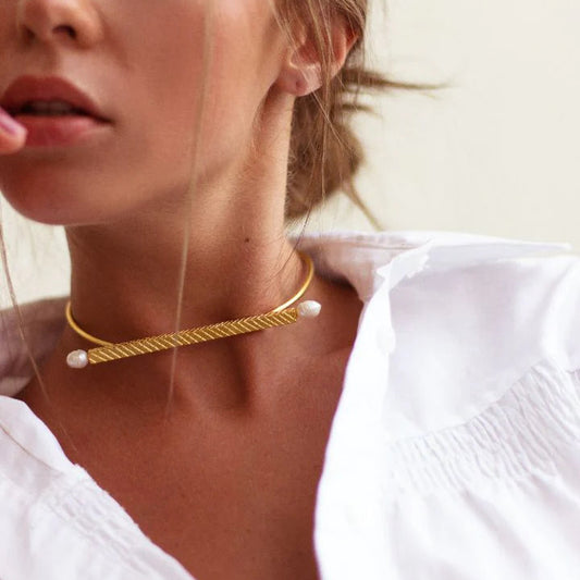 Woman wearing a gold choker necklace with pearls against a neutral background