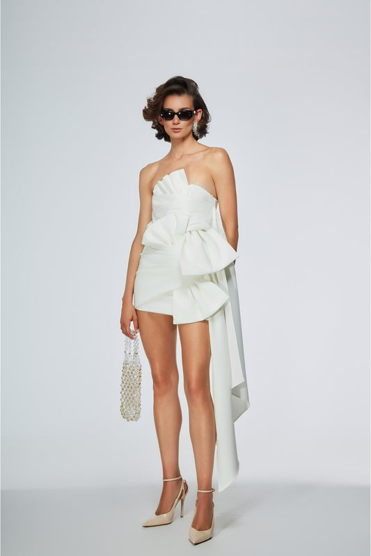Woman wearing a white strapless dress with a large bow detail on a plain background