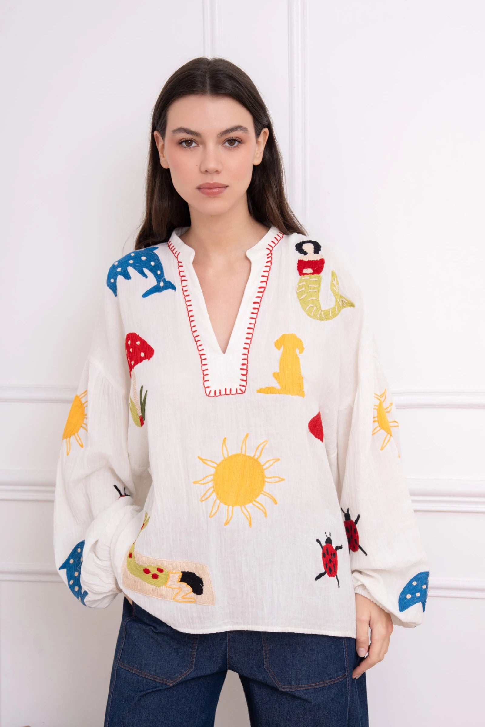 Woman wearing a white blouse with colorful embroidered designs against a white background