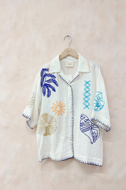 White cardigan with colorful embroidered designs on a beige background
