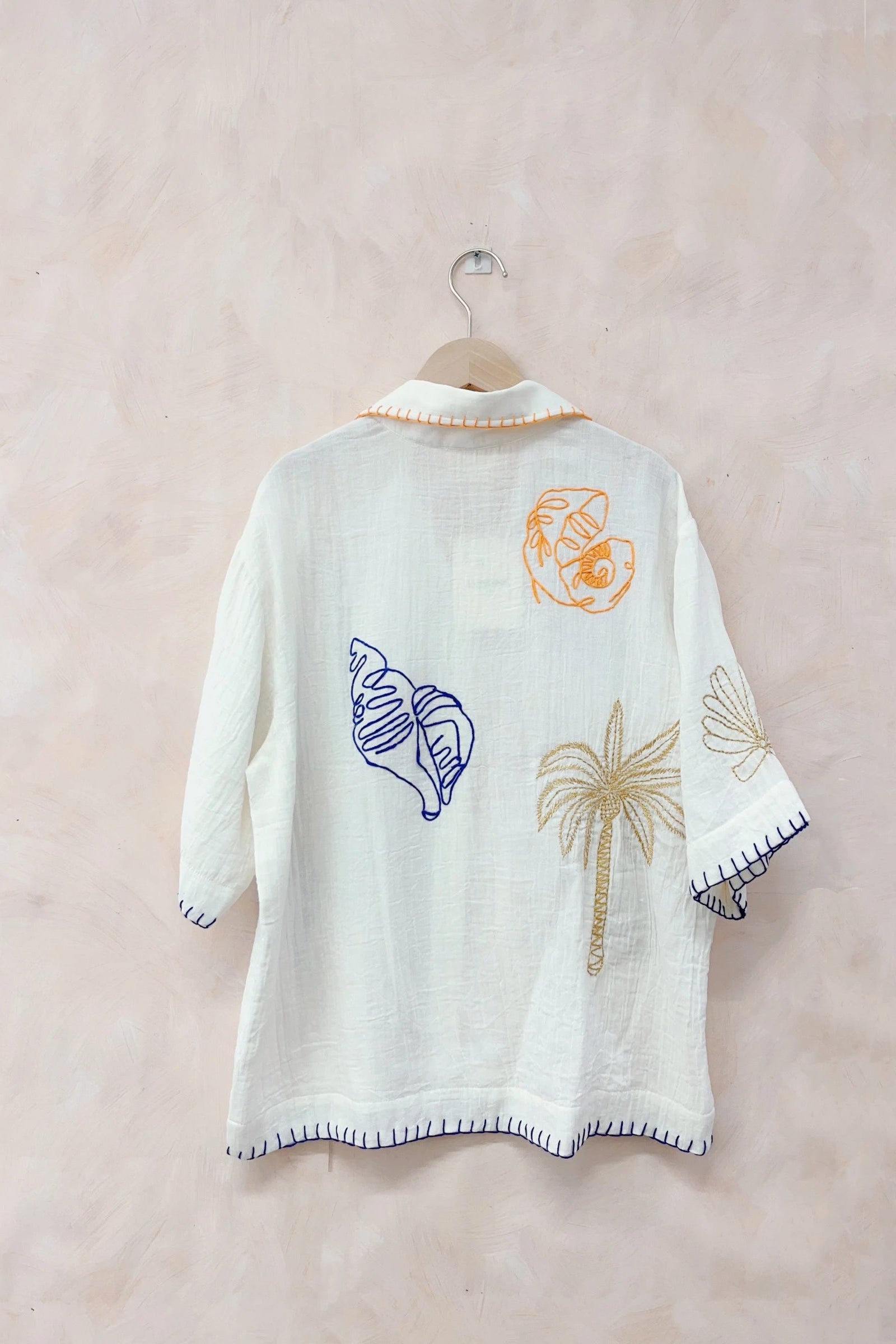 White embroidered poncho with shell and palm tree designs on a beige background