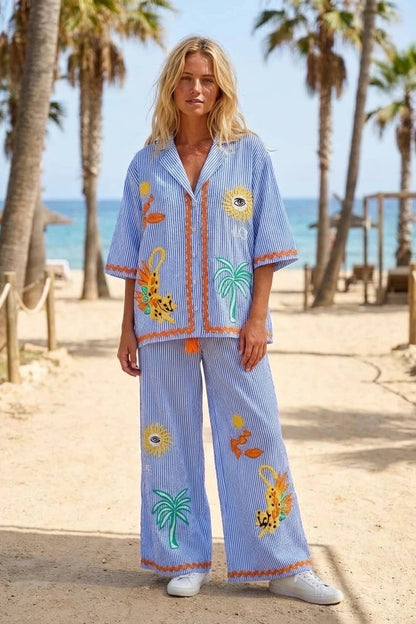 Woman in a blue embroidered outfit on a beach with palm trees and ocean in the background