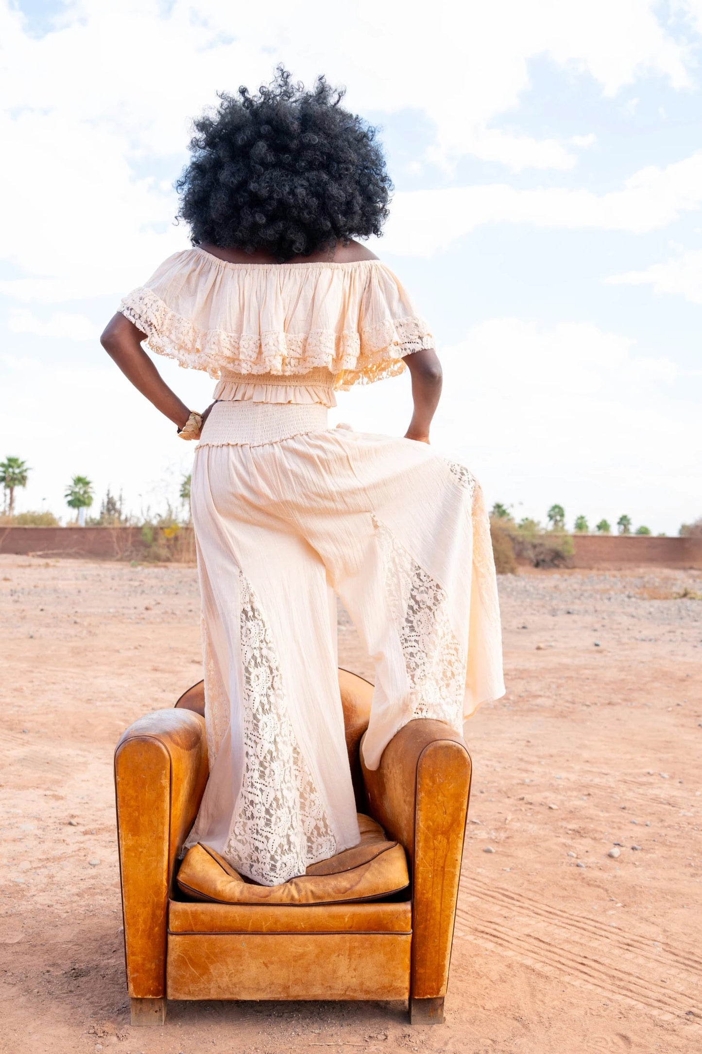 Person in a white dress sitting on a brown chair in a desert-like setting with a clear blue sky.