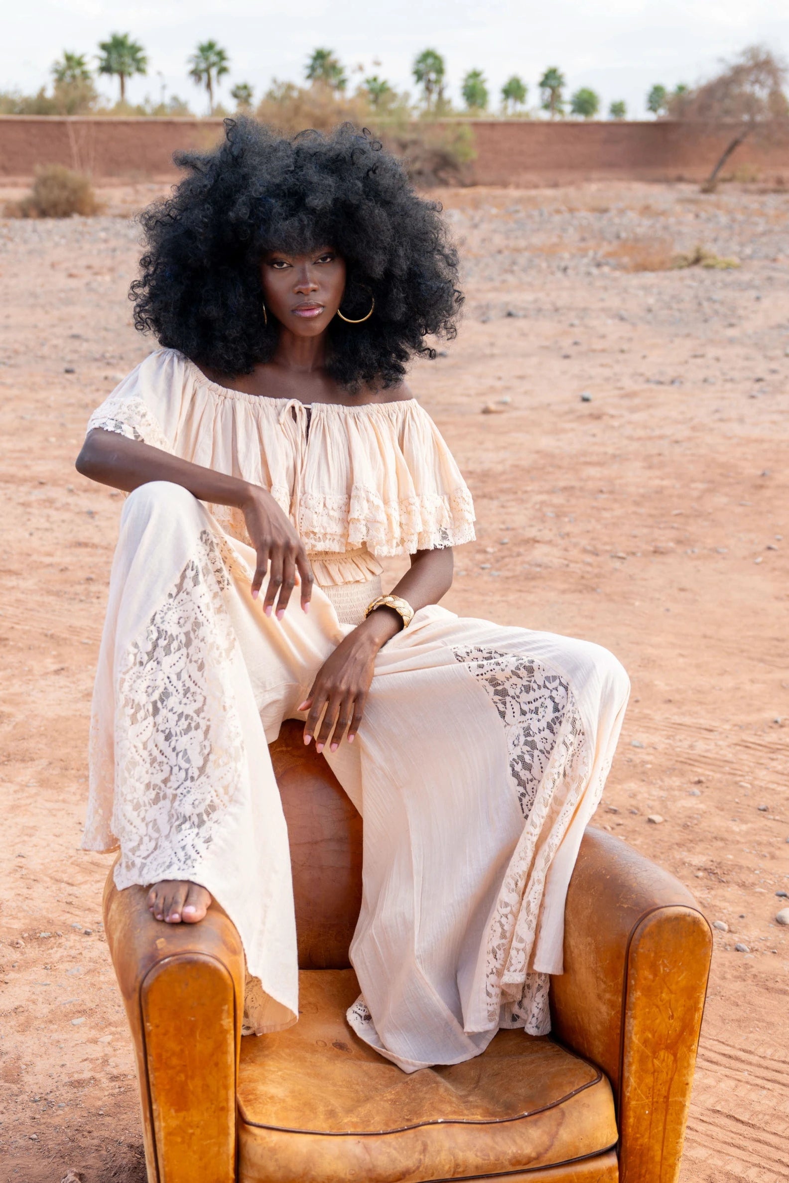 Woman in a flowing dress sitting on a leather chair in a desert setting